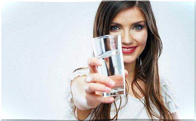 A woman holds a glass of water in front of her.